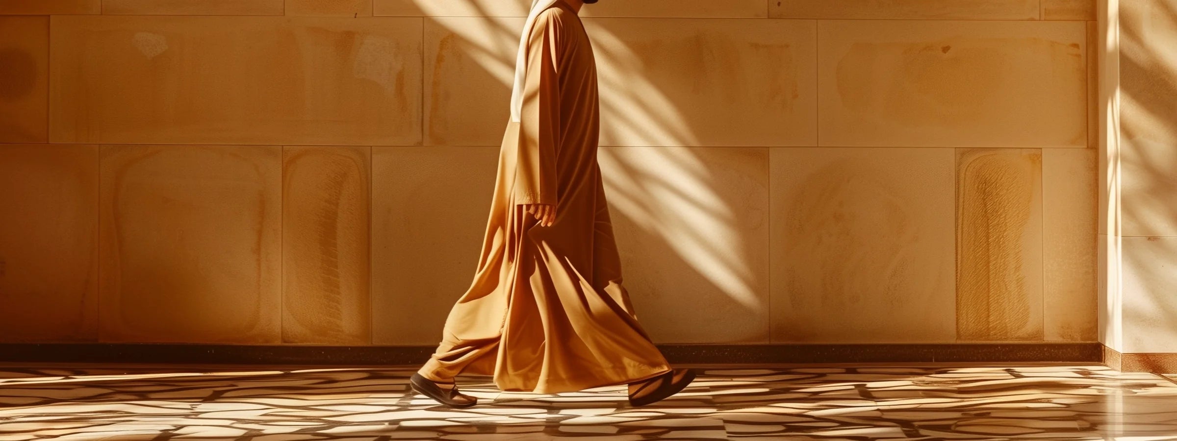 Arabische Herrenkleidung – Mann in elegantem sandfarbenem Thobe vor warmer orientalischer Architektur